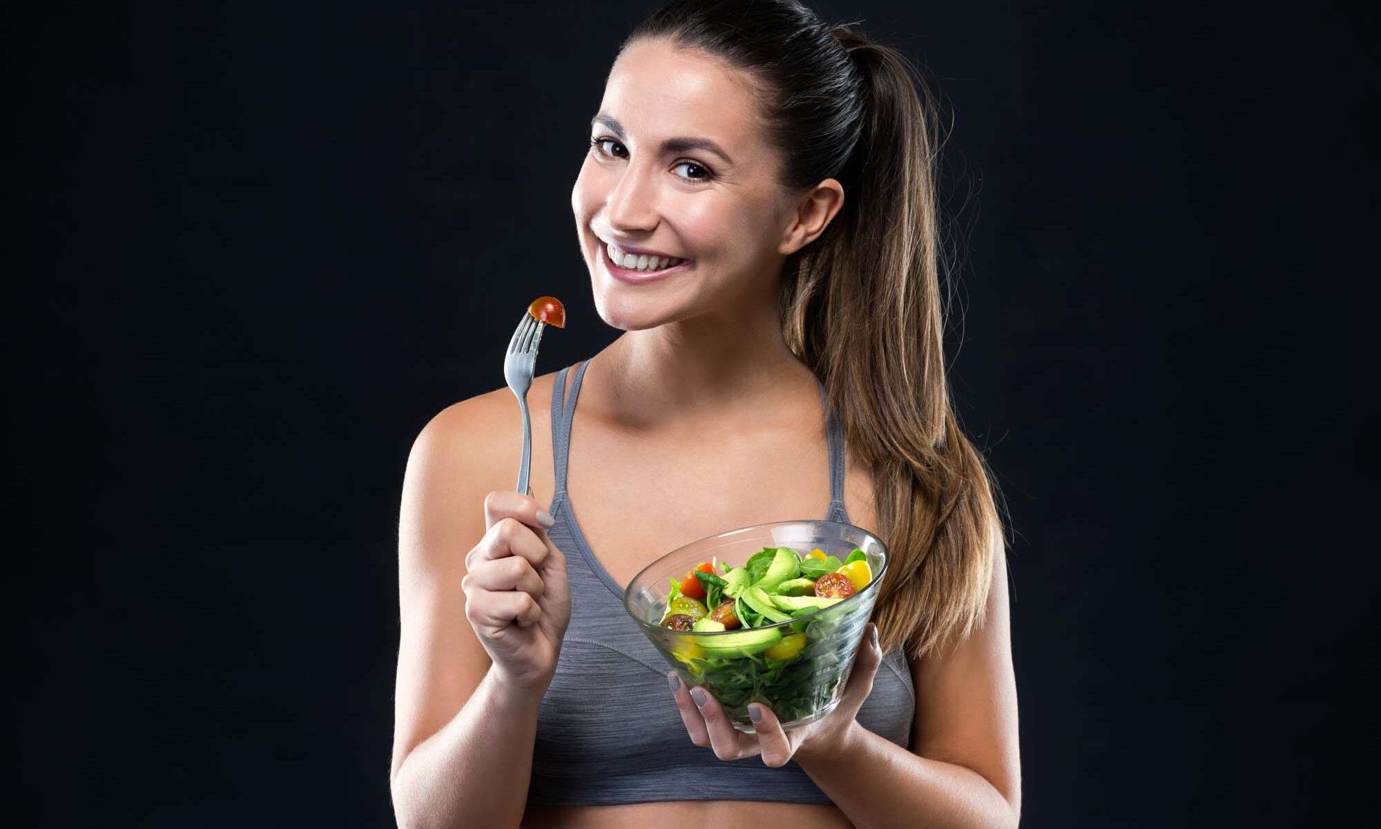 beautiful-young-woman-eating-salad-black-background (1)